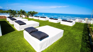 Outdoor lounge chairs on a grassy area with a view of the ocean and city skyline. - Iconic Rooftop, Bar & Gym | Luxe 2 BR at Soho PV (Puerto Vallarta)