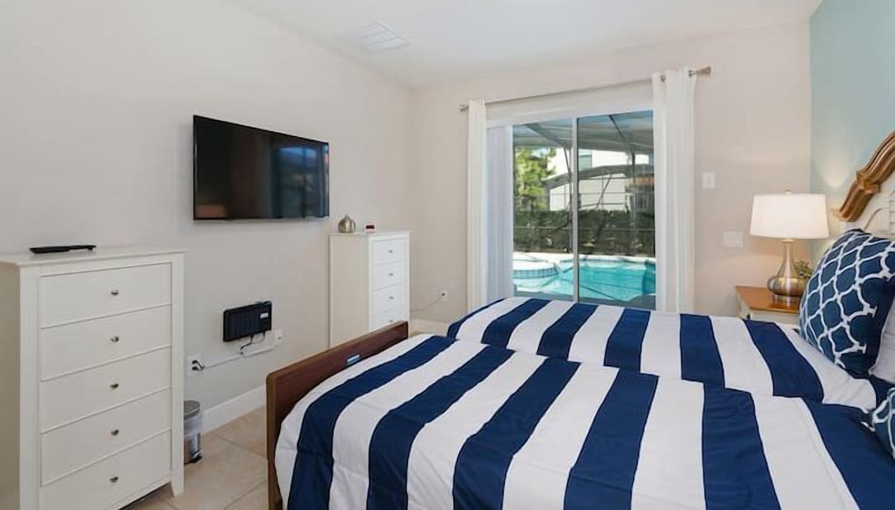 Une chambre à coucher comprenant un lit, une télévision, une commode, une table de chevet et donnant sur une piscine.