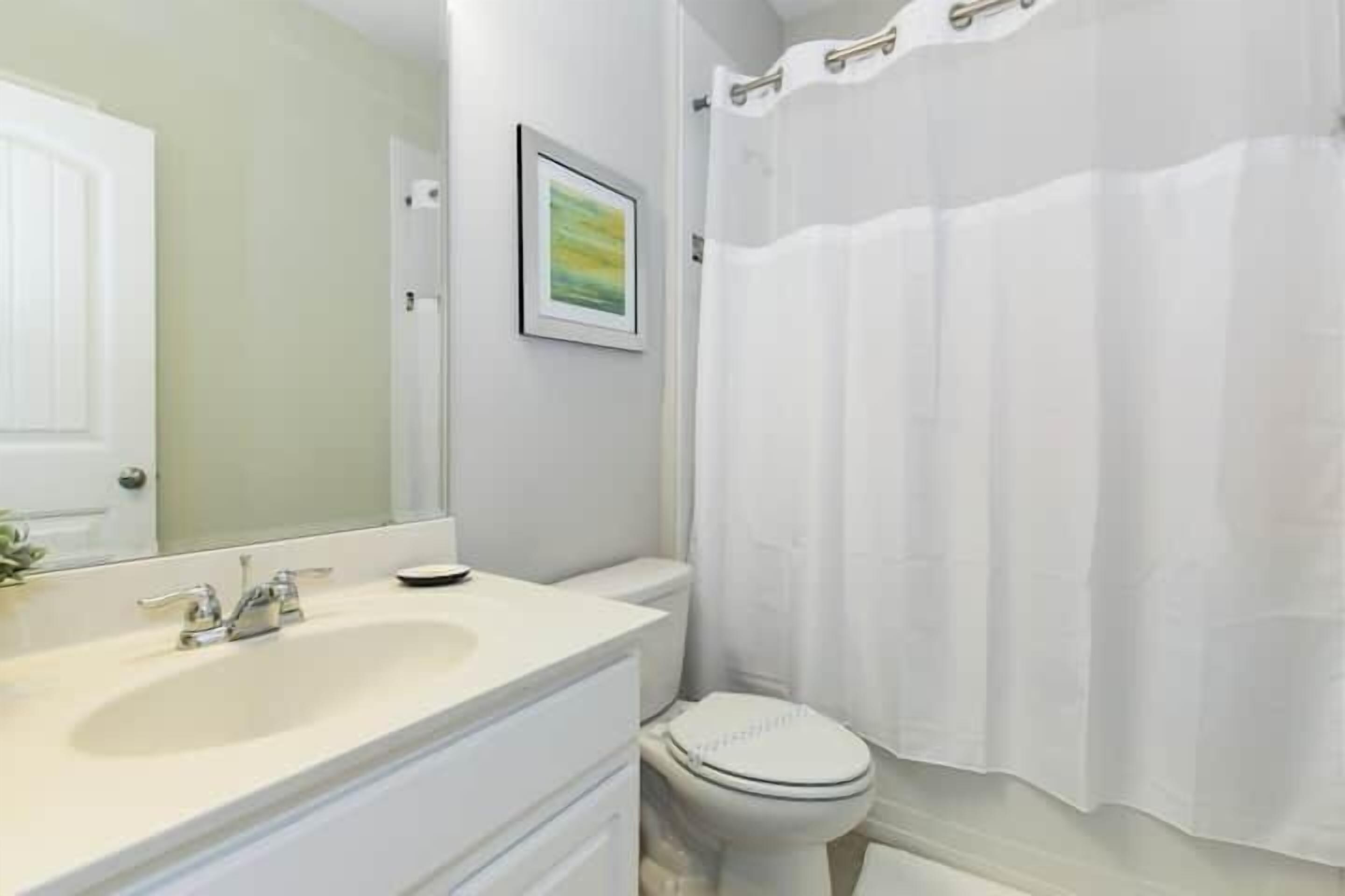 A bathroom with a white sink, mirror, toilet, and shower curtain.