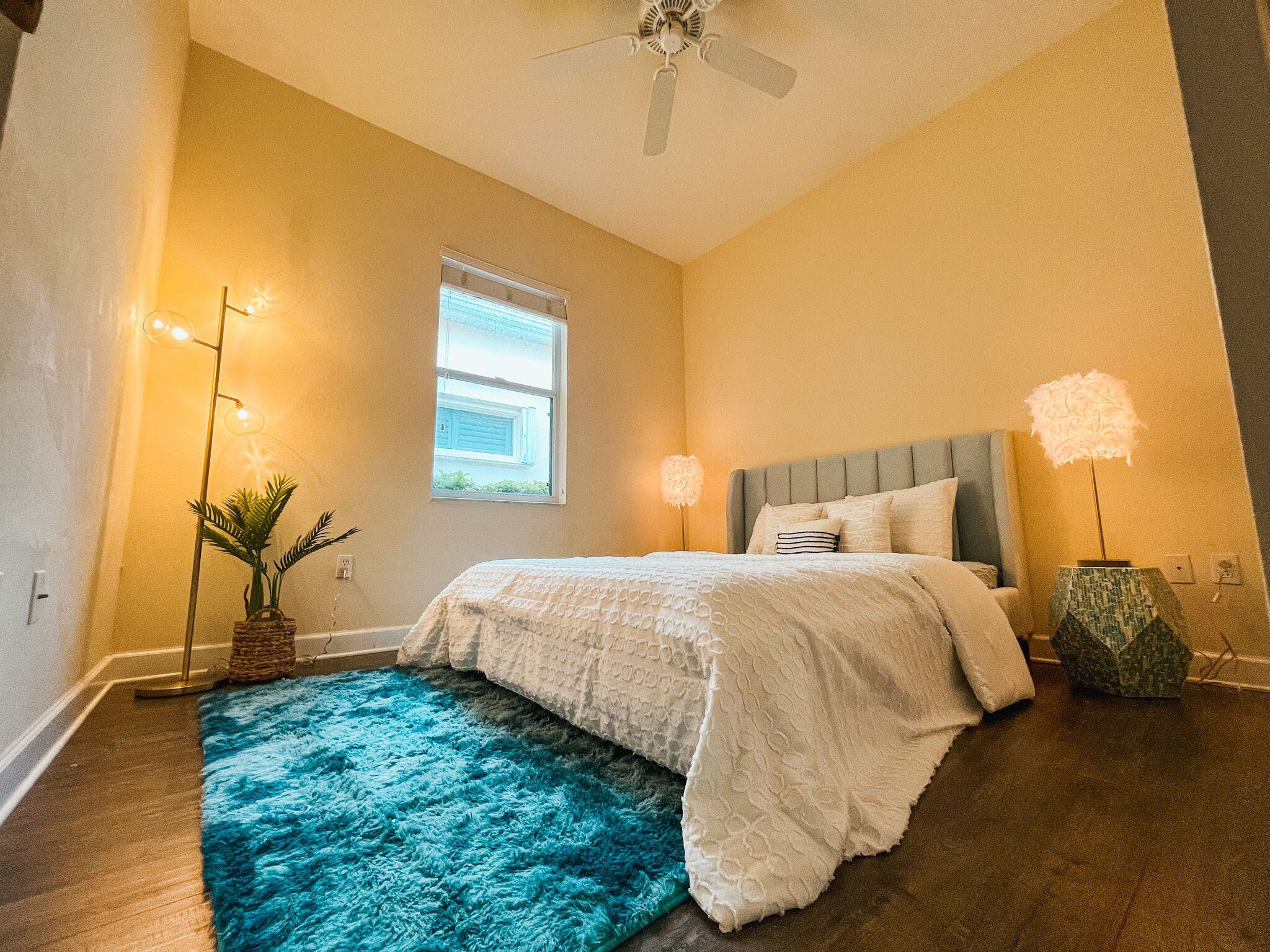 A bedroom with a bed, a ceiling fan, a window, and a blue rug.