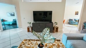 Ein Wohnzimmer mit einem großen Flachbildfernseher auf einem Schrank, einem Couchtisch mit einer Pflanze und einem blauen Sofa.