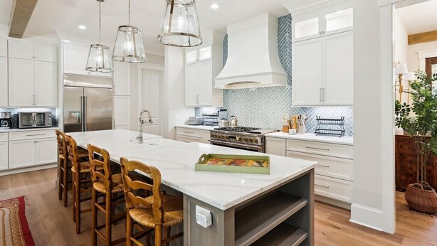 Una cocina moderna con armarios blancos, una isla grande con taburetes de bar, electrodomésticos de acero inoxidable e iluminación colgante.