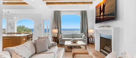 A spacious living room with a large window, a fireplace, and a television displaying a sunset scene.