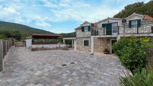 A two-story stone building with a covered patio, stone walls, and a view of a hill. - Villa Emanuel in Ljubitovica  - Haus für 4-6 Personen (Ljubitovica)