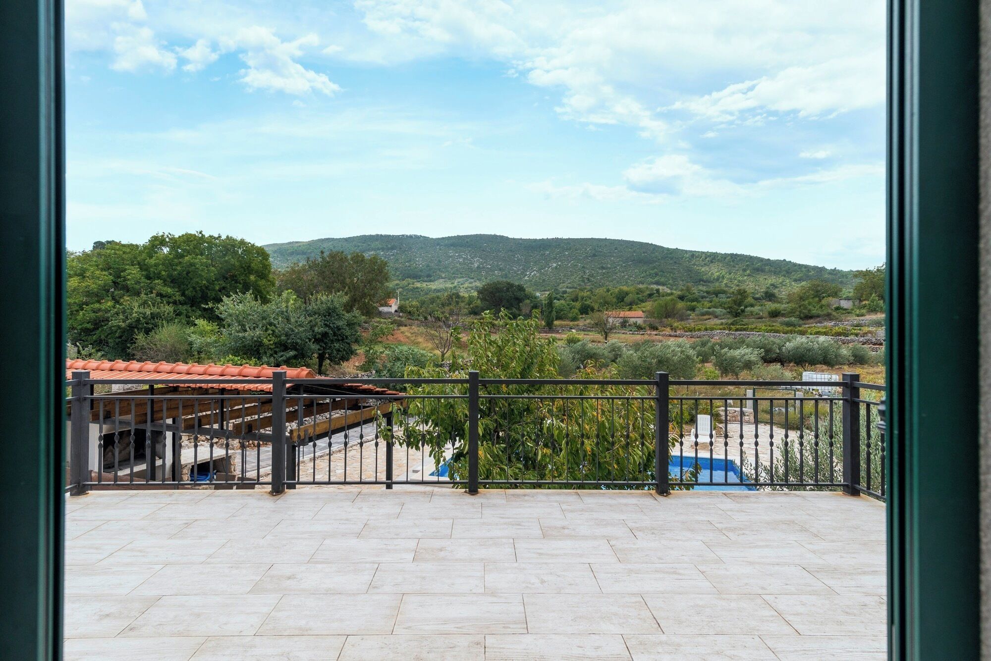 Un balcone con vista su un paesaggio collinare, pavimento in piastrelle e ringhiera in metallo.