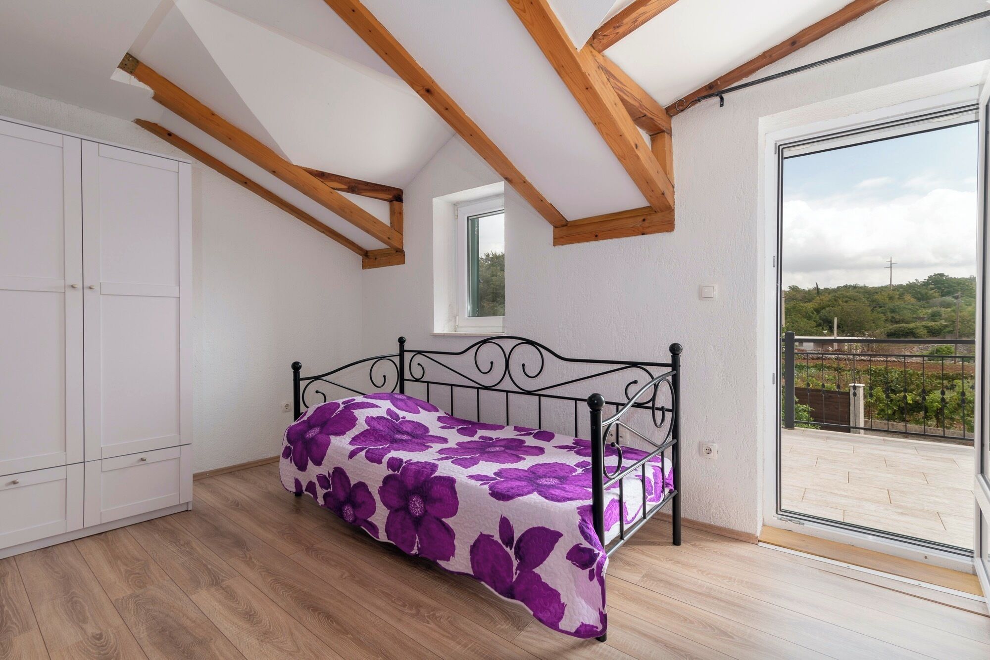 Ein Schlafzimmer mit Bett, Holzbalken, einem Fenster und einem Balkon mit Blick.