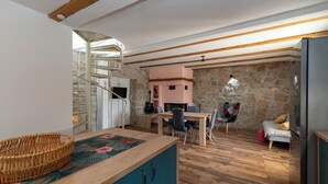 A cozy living room with a stone wall, a wooden ceiling, a dining table with chairs, a sofa, and a TV mounted on the wall. - Villa Emanuel in Ljubitovica  - Haus für 4-6 Personen (Ljubitovica)