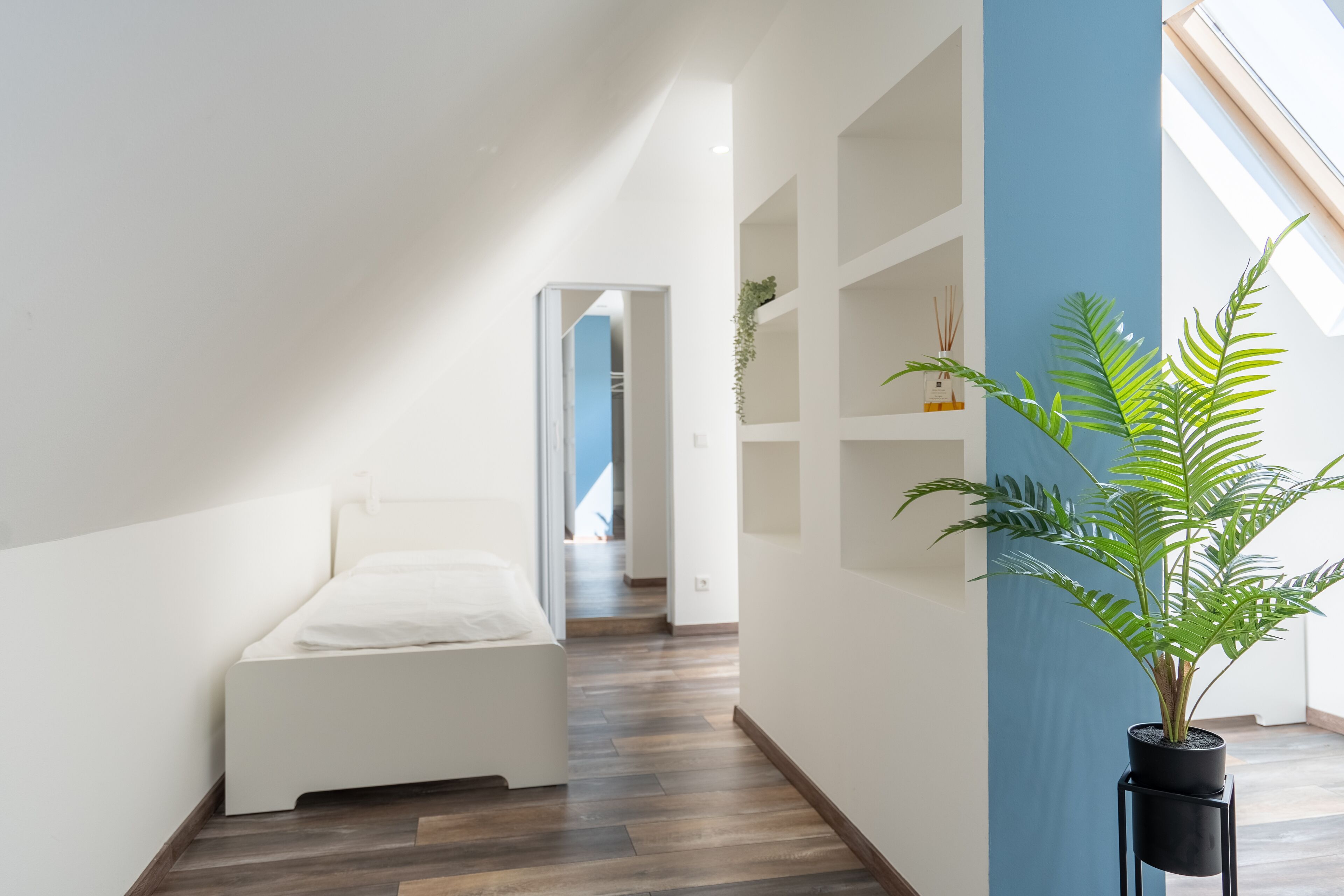 Une chambre moderne avec un lit, une plante en pot et une vue sur un couloir.