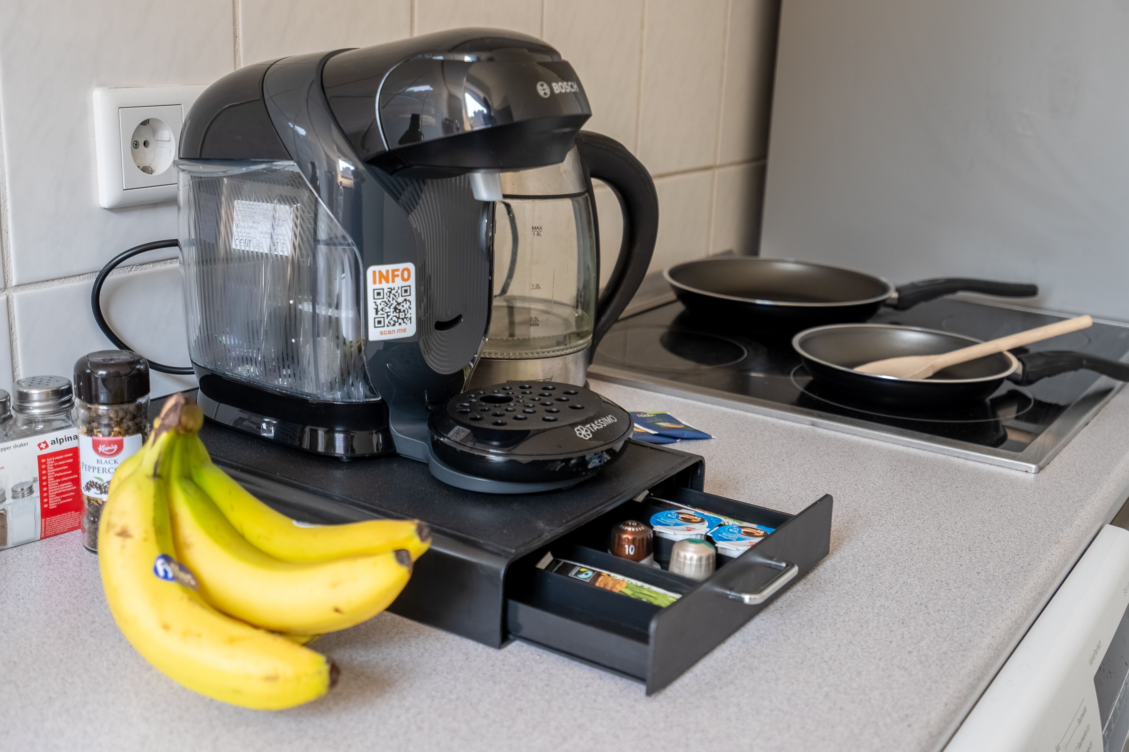 Een keuken met een koffiezetapparaat, een koekenpan, een houten lepel en een lade vol lekkernijen.