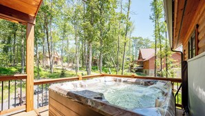 Eine Holzterrasse mit Whirlpool, umgeben von Bäumen und Blick auf Holzhütten.