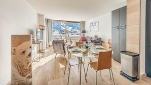 A modern dining area with a glass table, wooden flooring, and a view of a snowy landscape through large windows.