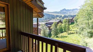 Un balcon doté d’une balustrade en bois, offrant une vue sur un paysage montagneux parsemé de maisons et de verdure.