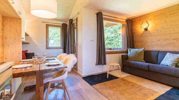 Un salon chaleureux avec un plancher en bois, un canapé, une table à manger avec des chaises et une fenêtre avec des rideaux.