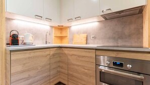 Une cuisine moderne avec des meubles de rangement en bois, un four encastré et une machine à café posée sur le plan de travail.