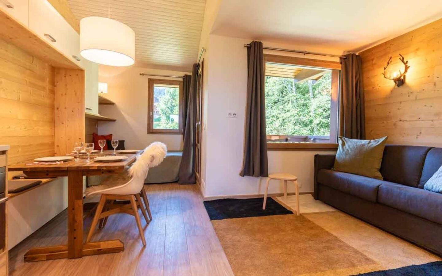 L’intérieur d’un chalet accueillant, avec un coin repas, un canapé et une fenêtre agrémentée de rideaux.