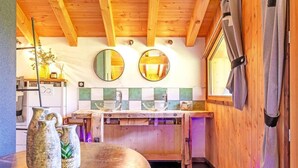 Une cuisine avec des poutres en bois, un plan de travail en bois et une fenêtre avec des rideaux. Il y a deux miroirs ronds accrochés au mur, ainsi qu’un évier avec un robinet.