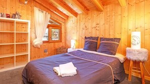 Une chambre dans une cabane en bois, avec un lit, une table de chevet, une étagère et une fenêtre.