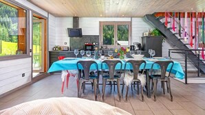 Un coin repas avec une table dressée pour six personnes, une cuisine en arrière-plan et un escalier agrémenté de décorations colorées.