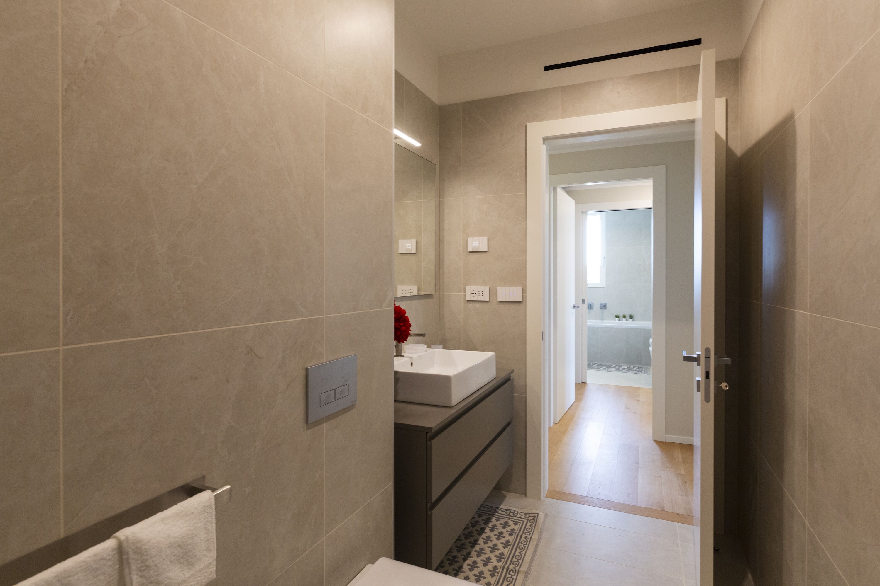 A modern bathroom with a large mirror, a white sink, and a towel rack.