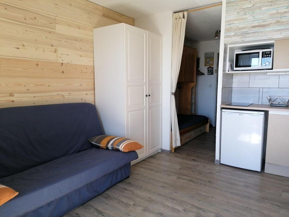 A compact room with a sofa, a wardrobe, a kitchenette with a microwave and a small fridge, and a wooden floor.