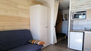 Una camera compatta con divano, armadio, angolo cottura completo di forno a microonde e piccolo frigorifero, e pavimento in legno.