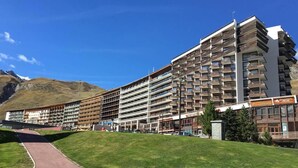 A multi-story hotel with a modern design, featuring a central courtyard and a mountain backdrop. - 10m from resort center, 11st floor, view lake, tv, ski locker, 12m², Tignes (Tignes)