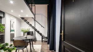 A modern interior with a staircase, a dining area with a round table and chairs, and a dark door. - E41 Boutique Apartments by BQA (Budapest)