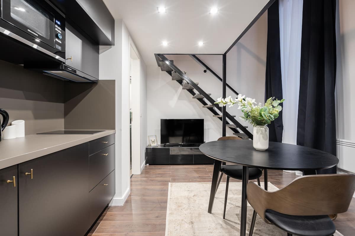 Une cuisine moderne avec des meubles de couleur sombre, un four à micro-ondes et un coin repas comprenant une table et des chaises.