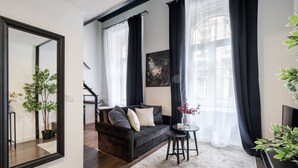 A modern living room with a dark sofa, a round coffee table, and a large mirror on the wall. - E41 Boutique Apartments by BQA (Budapest)