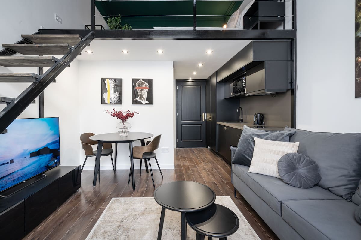 Un espace de vie moderne comprenant un escalier, un coin repas, une cuisine et un canapé gris.