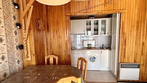 Une cuisine compacte aux murs en bois, une table à manger avec des chaises et un lave-linge.