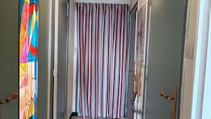 Un couloir avec un plafond en bois, des rideaux à rayures et un tableau abstrait aux couleurs vives sur le mur de gauche.