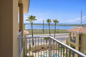 A balcony with a view of a swimming pool, palm trees, and a body of water. - Las Verandas 2 Bedroom Home by RedAwning (South Padre Island)