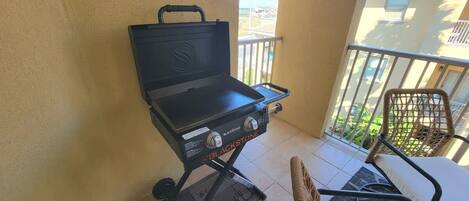 Una parrilla Blackstone en un balcón con una silla de mimbre y una mesa.