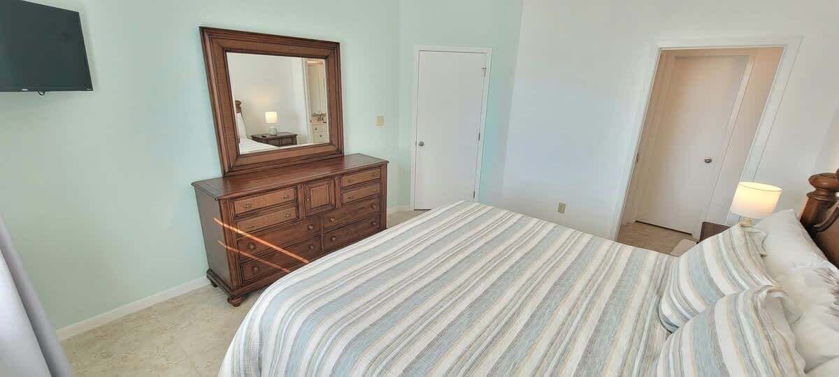 Een slaapkamer met een bed, een dressoir, een spiegel en een deur.