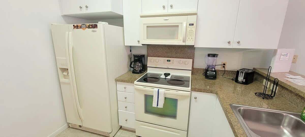 A compact kitchen with a refrigerator, microwave, stove, and sink.