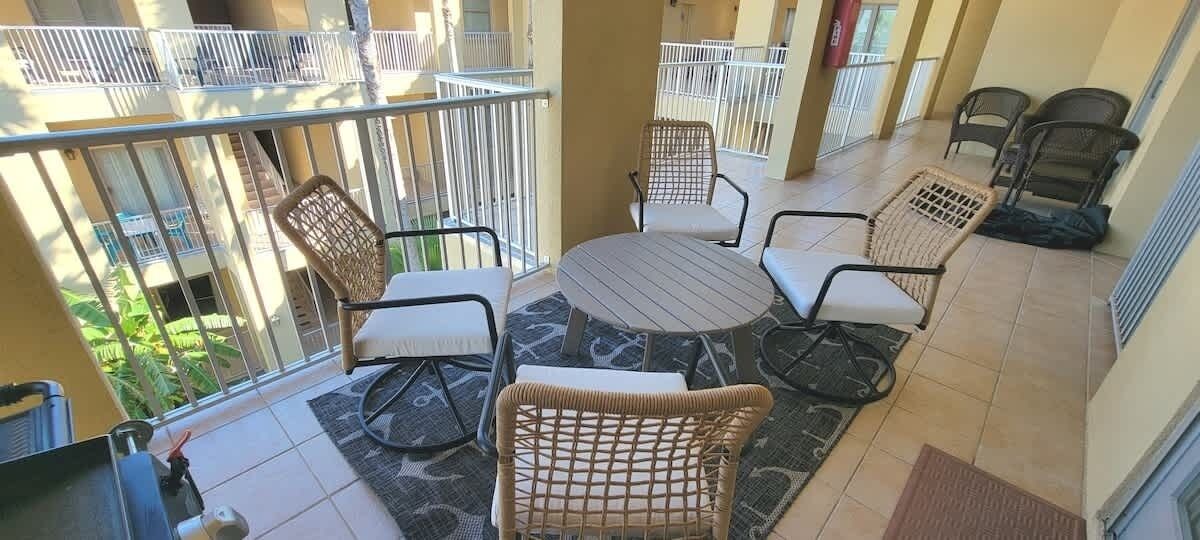 A balcony with wicker furniture, a round table, and a view of greenery.