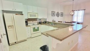 Una cocina con armarios blancos, encimera de granito, microondas, horno y pileta.