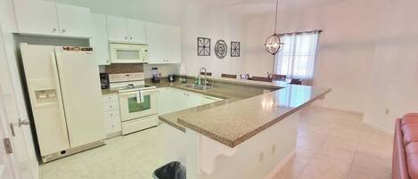 A kitchen with white cabinets, a granite countertop, a microwave, an oven, and a sink.
