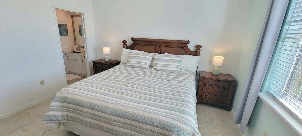 A bedroom with a large bed, two bedside tables, and a window with blinds.