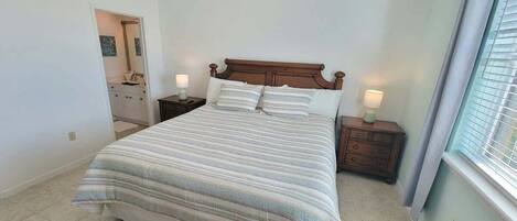 A bedroom with a large bed, two bedside tables, and a window with blinds.