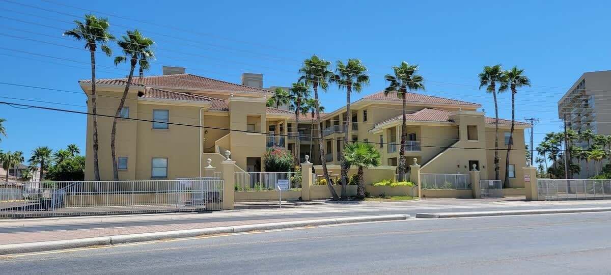 A multi-story building with a beige facade, palm trees, and a gated entrance.