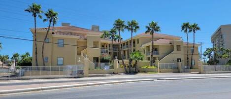 A multi-story building with a beige facade, palm trees, and a gated entrance.
