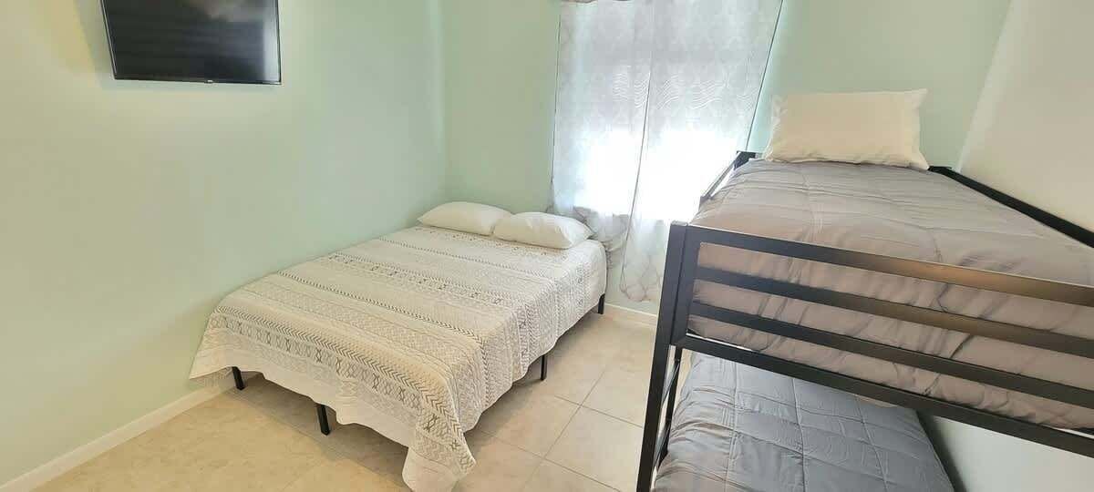 A bedroom with two beds, a window with curtains, and a flat-screen TV on the wall.