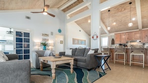 A spacious living room with a large sofa, a coffee table, and a dining area with wicker chairs. - Feelin' Salty - 107 Quebec 4 Bedroom Home by RedAwning (Dauphin Island)