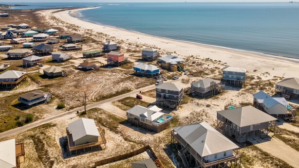 An aerial view of a coastal residential area with houses on stilts, a beach, and a clear sky. - Feelin' Salty - 107 Quebec 4 Bedroom Home by RedAwning (Dauphin Island)