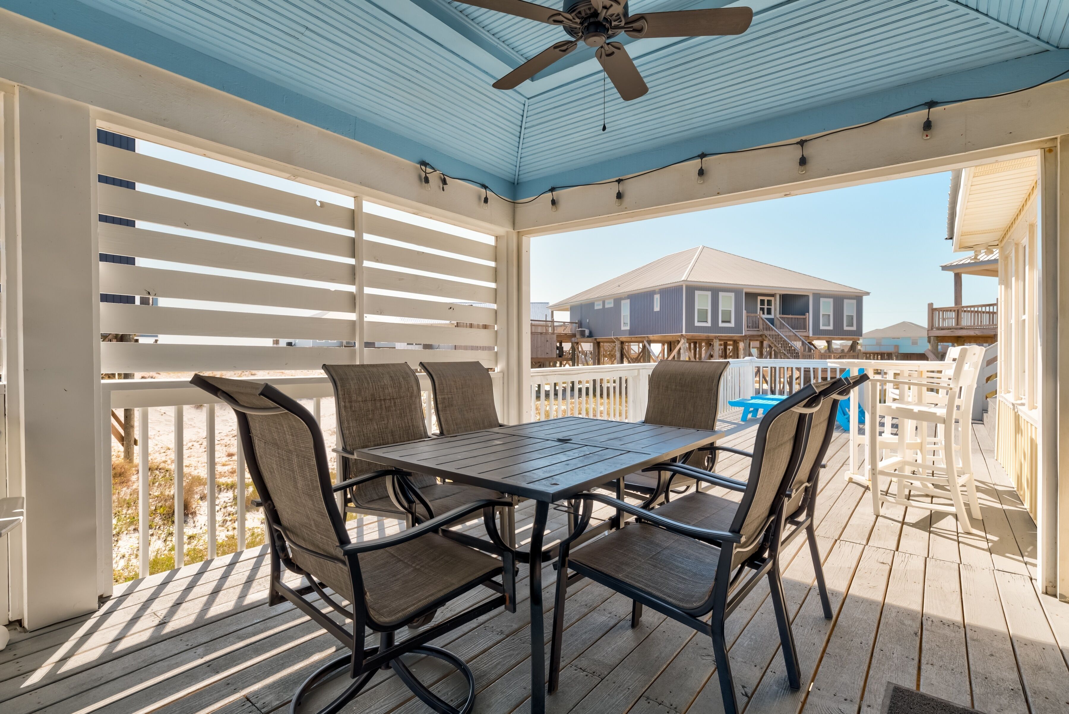 A covered outdoor patio with a table and chairs, a ceiling fan, and a view of a house in the background.