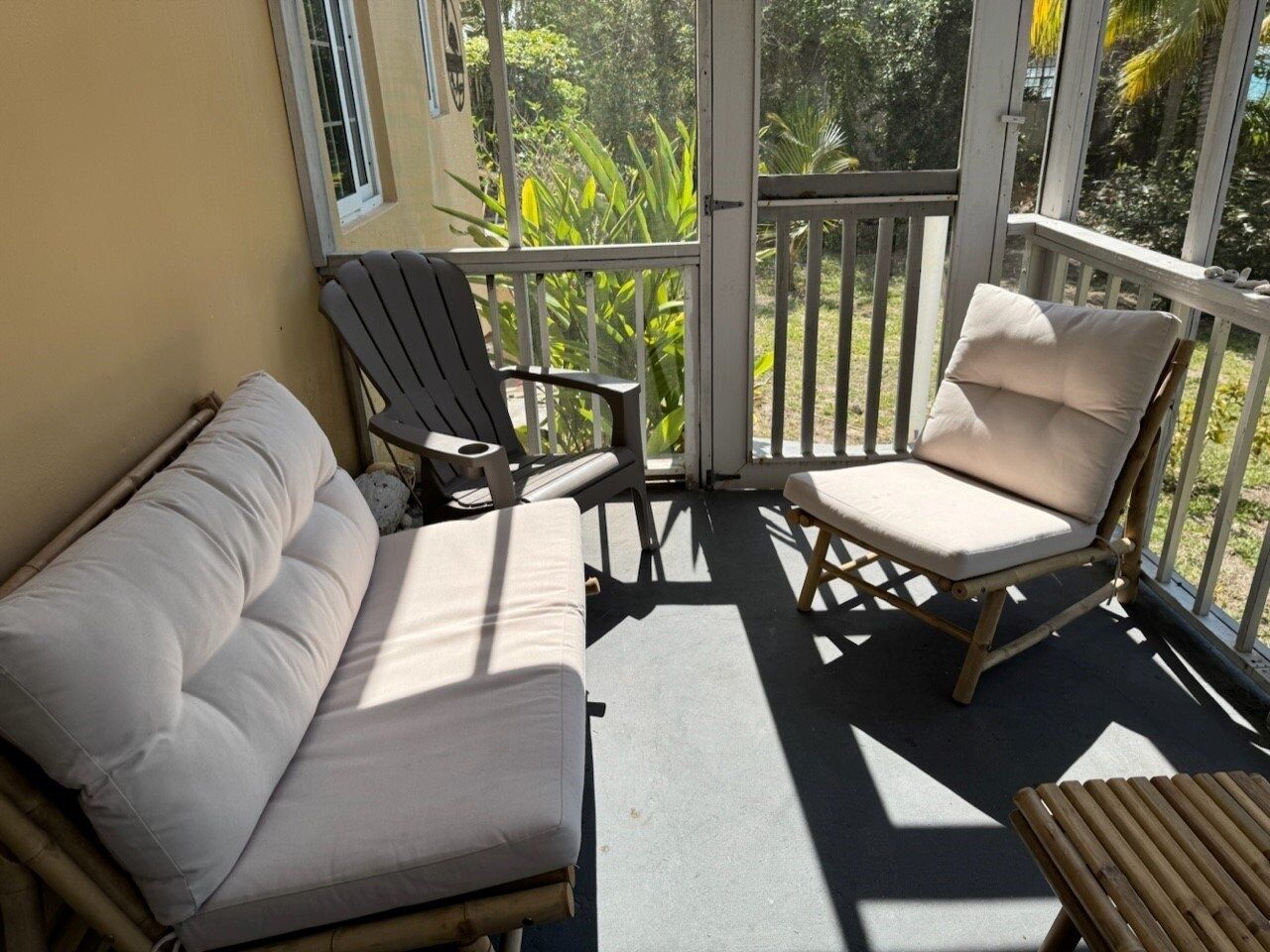 A sunlit balcony with a sofa, two chairs, and a small table.