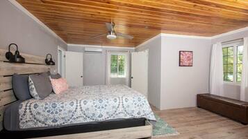Un dormitorio con techo de madera, cama con ropa de cama estampada, un banco y un ventilador de techo.