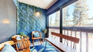 A balcony with a blue wall, wooden furniture, and a view of trees and a house. - Courchevel #5 2 Bedroom Condo by RedAwning (Mammoth Lakes)